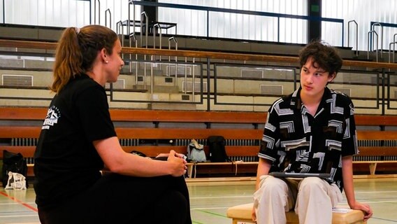 Zwei Personen sitzen in einer Sporthalle und unterhalten sich Zwei Personen sitzen in einer Sporthalle und unterhalten sich © Finja Ellermann Foto: Finja Ellermann