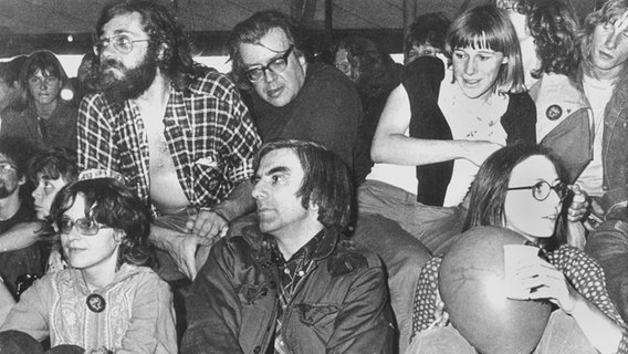 Rudi Dutschke (sitzend) und Erich Fried (stehend hinter Dutschke) in einer Gruppe von Menschen, die 1976 an einem Kongress in Frankfurt teilnehmen. © picture-alliance / dpa | dpa 