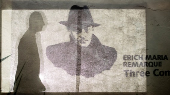 Ein Remarque-Graffiti mit dem Titel "Three Comrades" (Airbrush auf Mauer, 2014) des Künstlers Dr. Love/Bacha Koperia ist im Erich-Maria-Remarque-Friedenszentrum zu sehen. Im Hintergrund die Silhouette des Leiters Thomas Schneider. © picture alliance/dpa Foto: Friso Gentsch