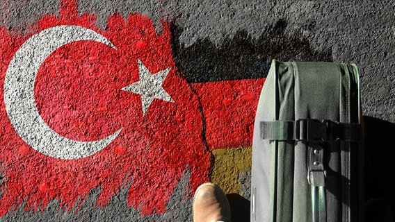 Koffer steht auf Asphalt, der mit einem Graffiti bemalt ist, das deutsche und türkische Flaggensymbole zeigt. © photocase, fotolia Foto: photographe, cil86