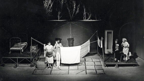 Schwarzweißbild: Gretchen (Bärbel Röhl) und der junge Faust (Horst Kotterba) vor einer Wäscheleine mit Mephisto (Lore Tappe) und Marthe (Ute Kämpfer)  
