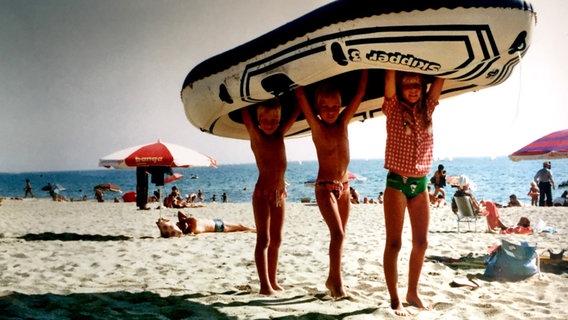 Drei Kinder stehen am Strand und halten ein Schlauchboot über ihren Kopf. © Katharina Mahrenholtz 