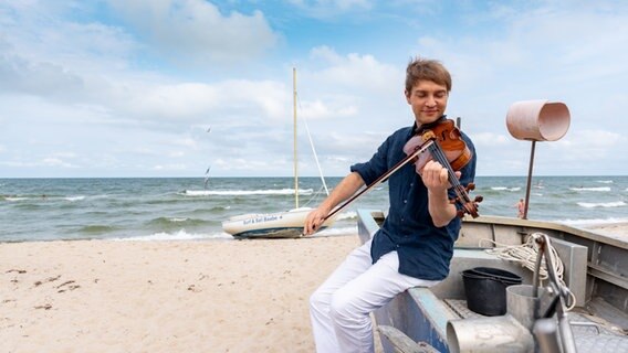 Nils Mönkemeyer spielt, gelehnt an ein Boot, Bratsche an einem Strand. © Holger Martens 