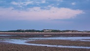 Das Wattenmeer bei Amrum im blau-rosigen Licht, dahinter sind Dünen zu erkennen © Zoonar.com/Rico Ködder Foto: Rico Ködder