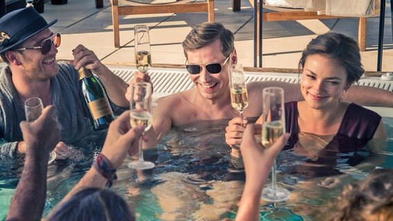 Frederick Lau (links) und David Kross (mit Sonnenbrille) und Janina Uhse (r.) mit Champagnergläsern in einem Pool - Szene aus der Netflix-Serie "Betonrausch" © Nik Konietzny (Netflix) 