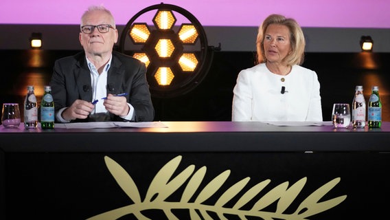 Eine Frau mit weißem Sakko und ein Mann mit Brille sitzen auf einem Podium bei der Pressekonferenz zur Bekanntgabe der Filme beim Filmfest Cannes 2025 in Paris © Michel Euler/AP/dpa +++ dpa-Bildfunk +++ Foto:  Michel Euler