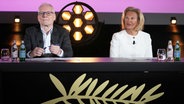 Eine Frau mit weißem Sakko und ein Mann mit Brille sitzen auf einem Podium bei der Pressekonferenz zur Bekanntgabe der Filme beim Filmfest Cannes 2025 in Paris © Michel Euler/AP/dpa +++ dpa-Bildfunk +++ Foto:  Michel Euler