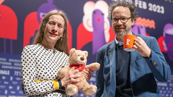 Mariette Rissenbeek hält einen Teddy in der Hand, Carlo Chatrian einen Berlinale-Becher - © Monika Skolimowska/dpa +++ dpa-Bildfunk +++ Foto: Monika Skolimowska