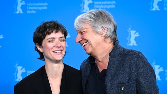 Regisseur Andreas Dresen und Liv Lisa Fries lachen zusammen vor blauer Berlinale-Wand vor der Premiere von "In Liebe, deine Hilde" © Soeren Stache/dpa +++ dpa-Bildfunk +++ Foto: Soeren Stache