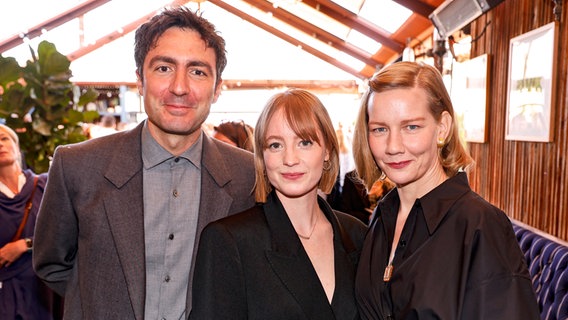 Regisseur  İlker Çatak (links) mit seiner Hauptdarstellerin von "Das Lehrerzimmer", Leonie Benesch (Mitte) und Schauspielerin Sandra Hüller (r.)  beim Oscars-Empfang der German Films in Los Angeles © German Films/ Kurt Krieger Foto: Kurt Krieger