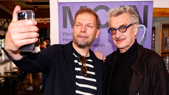 Moin-Geschäftsführer Helge Albers (links) macht ein Selfie vor einer lilafarbenen Wand mit Regisseur Wim Wenders (mit dunkler Brille, rechts) beim Oscar-Empfang der German Films in Los Angeles © German Films/ Kurt Krieger Foto: Kurt Krieger