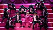 Ein Mann im pinken Anzug mit Sonnenbrille (Ryan Gosling) sitzt auf Stufen und singt "I'm just Ken" bei der Oscar-Gala mit vielen Männern mit Hut © AP Photo/Chris Pizzello Foto: Chris Pizzello