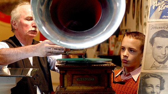 Ein alter und ein junger Mann hören eine Schallplatte auf einem Grammophon.  