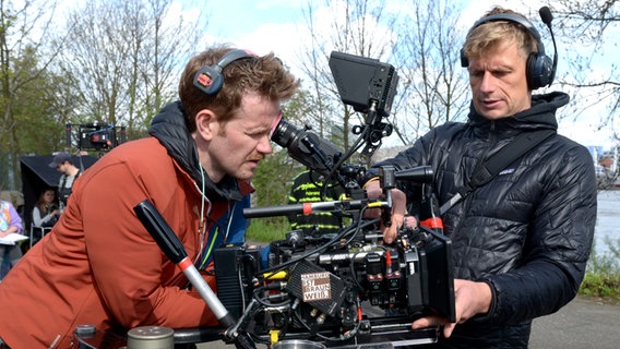 Ein Kameramann guckt durch den Sucher seiner TV-Kamera, der andere setzt ein neues Objektiv an die Kamera - Dreharbeiten am Hafen zum Spielfilm "Triage" der Serie "Großstadtrevier" © NDR Foto: Patricia Batlle