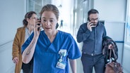 Eine Frau mit blauem Kittel telefoniert in einem Krankenhausflur, dahinter laufen zwei weiter Personen © Tobis Verleih 