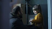 "Hide & Seek - Gefährliches Versteckspiel: Neue Partner": Jevgenij Borovko (Oleksandr Kobzar) steht in einer Wohnung seiner siebenjährigen Tochter Alina (Azalia Tkachuk) gegenüber, die auf einer Kommode sitzt. Sie schauen sich lächelnd und liebevoll an. © Honorarfrei - nur für diese Sendung inkl. SocialMedia bei Nennung ZDF und FILM.UA/© Hide & Seek 