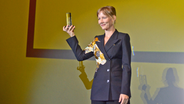Eine Frau in einem Kinosaal hält einen Preis hoch - Sandra Hüller erhält den Douglas Sirk Preis 2023 des Filmfests Hamburg © NDR Foto: Patricia Batlle