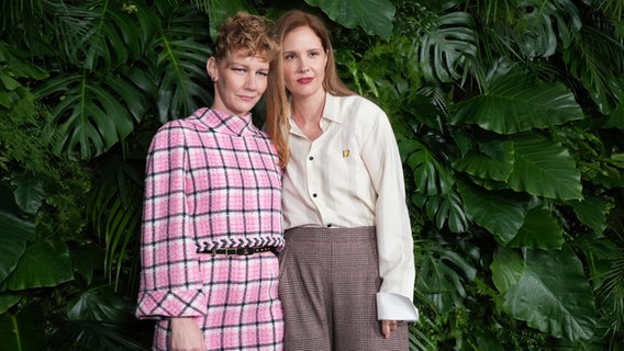 Schauspielerin Sandra Hüller (links) steht im rosa Chanel-Outfit neben Regisseurin Justine Triet (r.) vor grüner Pflanzenwand © Jordan Strauss/Invision via AP/dpa +++ dpa-Bildfunk +++ Foto: Jordan Strauss
