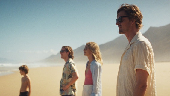 Szene aus dem Film "Islands": Vier Personen stehen am Strand und blicken aufs Meer © 2025 augenschein Filmproduktion / LEONINE Studios Foto: Juan Sarmiento G.