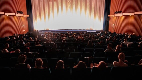 Ein Kinosaal, in dem Besucher vor einer beleuchteten Leinwand auf den Beginn des Films warten. © Paul Zinken Foto: Paul Zinken