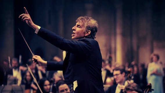 Bradley Cooper spielt Leonard Bernstein beim Dirigieren eines Orchesters mit erhobenem Arm im Film "Maestro" © Jason McDonald Netflix 2023 Foto: Jason McDonald