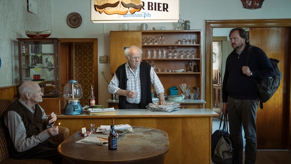 Szenenbild aus dem Film "Mittagsstunde": Drei Männer in einer Gasthof-Kneipe mit Tresen. Szenenbild aus dem Film "Mittagsstunde": Drei Männer in einer Gasthof-Kneipe mit Tresen. © Majestic / Christine Schroeder