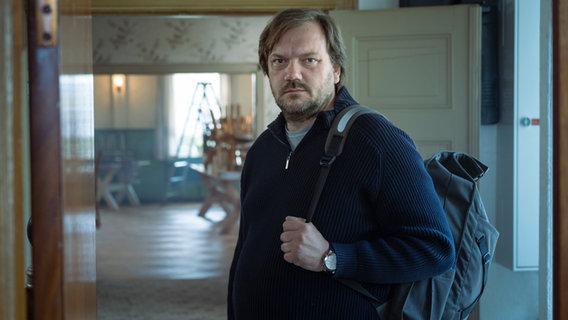 Szenenbild aus dem Film "Mittagsstunde": Ein Mann (Charly Hübner) mit Rücksack blickt in die Kamera. Szenenbild aus dem Film "Mittagsstunde": Ein Mann (Charly Hübner) mit Rücksack blickt in die Kamera. © Majestic / Christine Schroeder