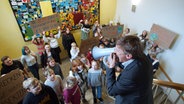 Szene aus dem Film "Muxmäuschenstillˣ": Ein älterer Mann spricht durch ein Megafon vor Schülerinnen und Schülern © Mux Filmproduktion / Ralf Noack 