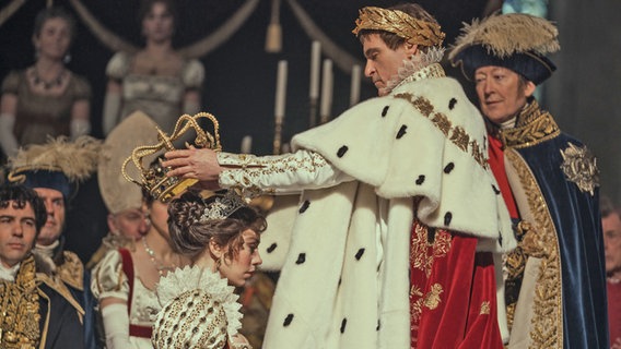 Ein Mann mit Kaiserkrone krönt eine Kaiserin (Joaquin Phoenix und Vanessa Kirby) - Szene aus Napoleon von Ridley Scott © Apple+ 