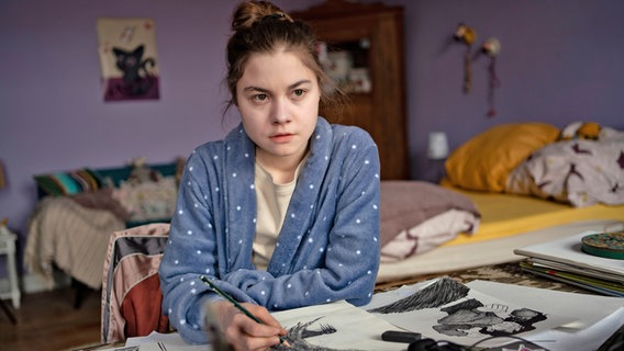 Eine jungen Frau sitzt in ihrem Zimmer und zeichnet düstere Figuren - Szene aus der Serie "Die nettesten Menschen der Welt" © NDR/Studio Zentral/Michael Ihle Foto: Michael Ihle