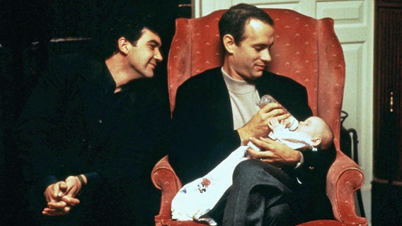 Tom Hanks gibt einem Baby eine Flasche, Antonio Banderas schaut liebevoll zu - Szene aus dem Hollywoodfilm "Philadelphia" von 1993 © Mary Evans  AF Archive Tristar Pictures / IMAGO Allstar 