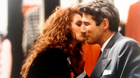 Eine roothaarige Frau küsst einen Mann mit Anzug auf die Wange. Filmszene aus "Pretty Woman" mit Julia Roberts und Richard Gere © picture alliance / kpa 