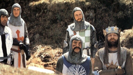 Mehrere Männer in schäbigen Ritterrüstungen schauen erwartungsvoll hoch - Szene aus "Ritter der Kokosnuss" von Monthy Python von 1975 © picture alliance 