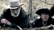 Szene aus dem Film "Rust - Legende des Westens": Ein älterer Mann und ein Junge liegen auf der Lauer. © 2025 RUST MOVIE PRODUCTIONS LLC, ALL RIGHTS RESERVED 