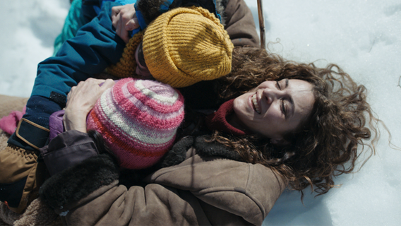 Szene aus dem Film "Sieben Tage": Eine Frau liegt mit zwei Kindern in ihren Armen im Schnee und lacht. © bravenewwork 