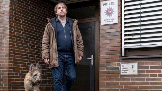 Sörensen (Bjarne Mädel) mit Hund Cord vor der Wache des Polizeireviers in Katenbüll - Szene aus "Sörensen hat Angst" von und mit Bjarne Mädel © NDR Foto: Michael Ihle