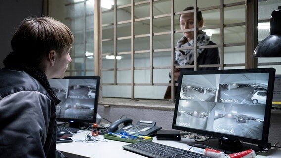 Ein Mann (Schauspieler Joseph Bundschuh) sitzt vor Überwachungskamera-Bildschirmen und spricht mit einer Frau (Schauspielerin Mathilde Bundschuh) hinter einem Gitter. © NDR Foto: Christine Schroeder