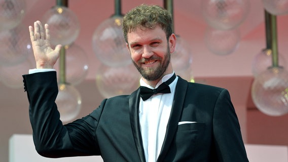 Un giovane con la barba in smoking sorride e saluta alla première del suo film a Venezia -  "La teoria di tutto" Scritto da Tim Krueger © imago Stock / Ettore Ferrari Foto: Ettore Ferrari