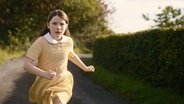 Ein Mädchen in gelbem Kleid und wehenden Haaren läuft einen Weg hinunter © Neue Visionen Filmverleih 