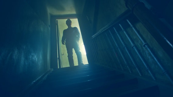 Ein Mann steht im Gegenlicht und blickt eine dunkle Treppe hinab - in einer Filmszene aus "Tian - Das Geheimnis der Schmuckstraße"  "Nordlichter"-Mysteryfilms von Damian Schipporeit © Fiction 2.0 für NDR 