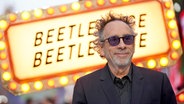 Ein Mann mit dunkler Brille lächelt von einem Neon-Schild zum Film "Beetlejuice, Beetlejuice" © Foto: Yui Mok/PA Wire/dpa +++ dpa-Bildfunk +++ Foto: Yui Mok