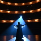 Eine Frau (Danielle Macdonald) steht mit geöffneten Armen auf einer Bühne im Scheinwerferlicht © 24 Bilder 