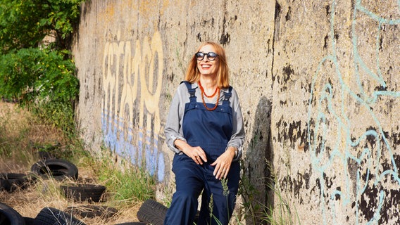 Die Künstlerin Gudrun Gut steht vor einer mit Graffiti besprühten Mauer. © RBB Foto: Mara von Kummer