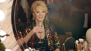 Comedy-Ikone Deborah Vance der Star einer täglichen Show im Palmetto Casino in Las Vegas sitzt mit einem Glas Champagner vor dem Spiegel eines Schminktisches. © ZDF 