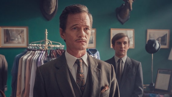 Szene aus "It's a Sin": Zwei Männer stehen in einem Geschäft voller Anzüge und schauen konzentriert in die Ferne. © ZDF und Ben Blackall 