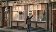 Ein Mann repariert den Schriftzug "The Old Oak" über einem Pub © picture alliance/dpa/Wild Bunch Germany | - 