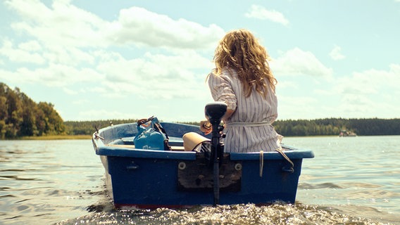Man sieht Schauspielerin Petra Schmidt-Schaller von hinten in einem Motorboot auf einen See hinausfahren. © NDR/Polyphon Foto: Philipp Sichler