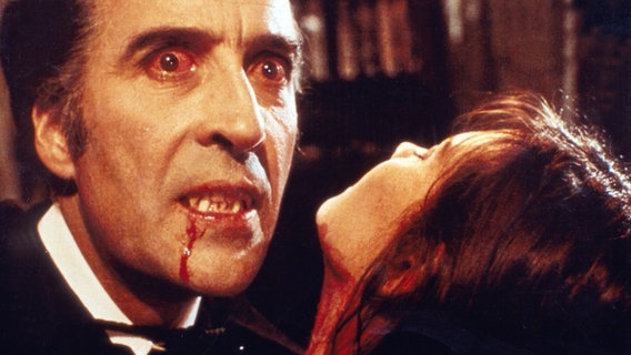 Ein Mann mit rotunterlaufenen Augen und blutigem Mund hält eine Frau im Arm (Christopher Lee als "Dracula") © picture alliance/United Archives | IFTN 
