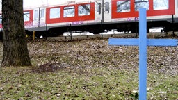 Blaues Gedenkkreuz am Unglücksort neben Bahnschienen. © NDR/PIER 53 Filmproduktion/Hauke Wendler 