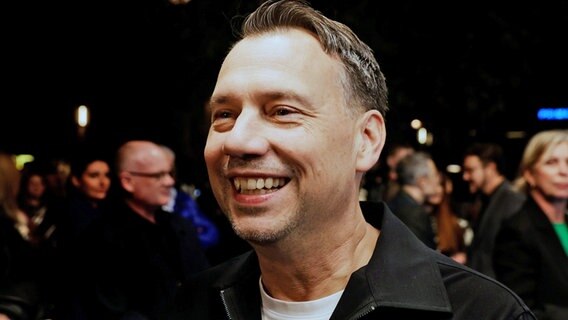 Sebastian Fitzek steht in einer Menschenmenge und lächelt. © Carsten Koall/dpa 